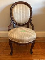 Front view of antique wooden lady's chair with upholstered seat and back, shows carved wood frame and cream patterned upholstery.