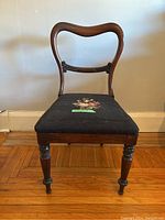 Front view of antique wooden chair showing curved upper backrest and navy blue needlepoint seat with floral embroidery.