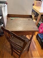 View from above and back of antique wooden child's desk showing slanted top and part of wooden chair seat.