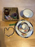Overview of all items in the lot on a wooden table including the floral china set, small basket with miniature pitchers and bird figurines, and turkey cookie cutter