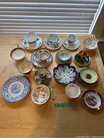 Assorted tea cups, saucers, small bowls, some with gold accent and floral patterns, various colors including green and maroon