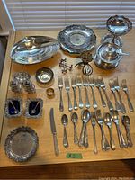 Full overview of assorted silver plate items arranged on table including dishes, candy dishes, tureen, salt and pepper shakers, and flatware.