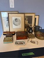 Wide view showing assortment of vintage items on table including framed pictures, boxes, metalware, basket and small collectibles.