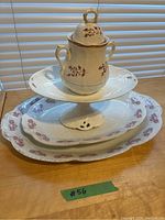 View of two large white oval platters with pink floral border, one smaller white pedestal dish, and white lidded jar with two handles and brown floral pattern
