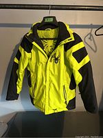 Front view of the child sized 18 Spyder ski jacket showing bright yellow with black accents, zippered pockets, spider logo on chest, hooded