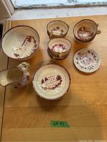 Overview of assorted cream-coloured china including teacups, saucers, small pitcher, and bowl with pink and gold painted design.