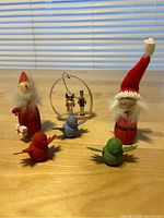 Small wooden holiday figurines including two gnomes with beards and red hats, three small colorful birds, and a wooden circular ornament with two soldier figurines inside.