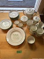 Full set arranged on a wooden table showing all various pieces in white china with green and lilac peacock feather designs.