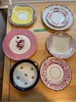 Top view showing six fine china platters in various colors and floral designs on wooden surface.
