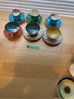 Top view photo showing all six teacups and saucers arranged in two rows. Variations in color and pattern visible.