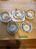 Top-down view of five tea cup and saucer sets arranged on a wooden surface showing varied floral and gold trim designs.