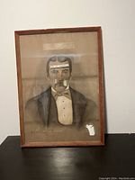 Framed image of a man behind glass, with visible stickers and remnants, frame shows damage especially on the lower right corner.