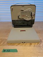 Front view of Kodak Brownie 500 projector inside its removable beige cover on wood table.