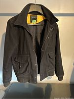 Black wool men's jacket hanging on a hanger, showing front details with pockets and collar.
