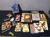 Photo showing a collection of assorted notebooks, notepads, novelty stationery items, and an iPhone case with colorful designs spread on a black surface.