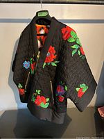 Front side of the reversible kimono style jacket showing black quilted fabric with large colorful flowers in red, green, blue, and purple.