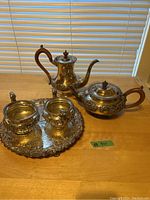 Full set of silver plated coffee pot, tea pot, sugar bowl, creamer, and tray shown from front view on wooden table with window blinds in background.
