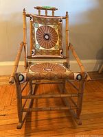 Front view of the small wooden rocking chair showing needlepoint embroidery on seat and backrest with a round geometric design and wooden frame.