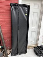 Soft vinyl tri-fold tonneau cover folded vertically, showing black vinyl surface and lightweight metal frame.