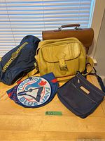 Photo showing six assorted vintage bags including vinyl and fabric, sports-related and university-branded duffels, attaché case, and shoulder bags.