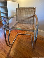 Front view of chrome cantilever chair with woven wicker seat and back on hardwood floor