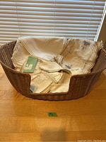 Wicker dog bed filled with cream/off-white antique linens on a wooden table.