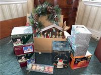 Lot overview showing boxed mugs, wreath, nativity scene, plastic egg boxes, hurricane lamp and other items