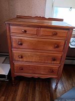Front view of vintage wooden 5-drawer dresser with wooden knobs and carved legs