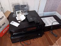 Photo showing stacked Harman Kardon AVR 20II receiver, Onkyo CD changer and cassette deck units with remote controls and white earphones on top