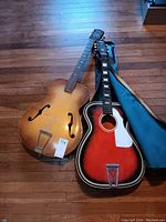 Shows both guitars side by side: brown Silvertone archtop and red sunburst Stella acoustic, both missing strings, with soft case.