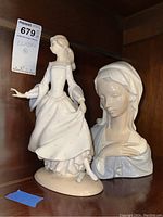 Two Lladro porcelain figurines together on a wooden shelf, the dancing woman on the left and the bust on the right.