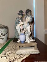 Three porcelain geisha figurines on display: kneeling figure with vase and two standing figures