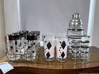 Tray holding twelve clear glass tumblers decorated with silver polka dots and silver rims, alongside frosted diamond-star tumblers, shot glasses and cocktail shaker