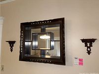 Front view of the rectangular wood framed mirror with ornate edge carvings mounted on a wall, flanked by a pair of matching wood sconce shelves with decorative scroll cutouts.