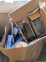 Open box containing air purifiers, brushes, twine and other household supplies.