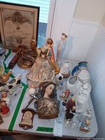 Table display showing religious figurines including Madonna, praying child, saint statues, ceramic animals, and framed marriage certificate