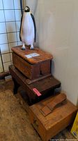 Photo showing the carved wooden penguin standing on the vintage wooden shoeshine box with one low wooden stand visible beneath.