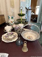 Full lot shot including porcelain teacups, saucers, Italian pitcher, metal bells, candy dish, and three-tiered stand.