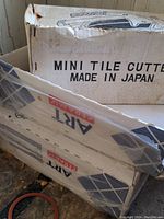 Photo showing two boxes labeled 'Mini Tile Cutter Made in Japan' containing tiles and tile cutter.