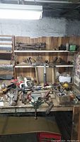 Overview of a workbench filled with assorted vintage hand tools including hammers, hand drills, clamps, tin snips and socket sets with wooden paneling background.
