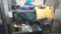 Metal shelving unit in basement with various tools and hardware including cardboard boxes of nails, screws, files, rotary file, and saw blades.