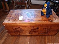 Top view of wood chest with rodeo artwork and plush dog on top, showing fading and scratches.