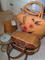 Wide view photo showing the three woven bags/baskets and two clocks arranged on floor with white cabinetry background