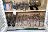 Cabinet shelf holding various mid-century clear glassware with black designs and gold-trimmed glasses.