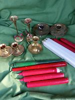Seven brass candlesticks of varying sizes and designs arranged with red, white, and green tapered candles on green fabric background.
