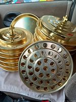 Photo showing several brass stackable communion trays and containers with cross handles on lids and plastic inserts.