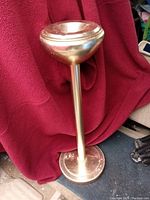 Full view of the brass floor ashtray standing on a red cloth background, showing the base, stem, and removable ash holder bowl at the top.