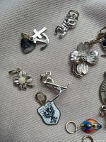 Photo showing assorted charms including heart-shaped cross and anchor, cherub, flowers, shield marked Henry, figure with rifle, small ring, and planet charm