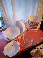 Overview of five Corningware casserole dishes stacked and arranged with at least two visible glass lids, showing different floral patterns on the ceramic cookware.