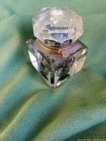Clear crystal square inkwell with faceted crystal lid and metal ring attachment resting on green fabric.
